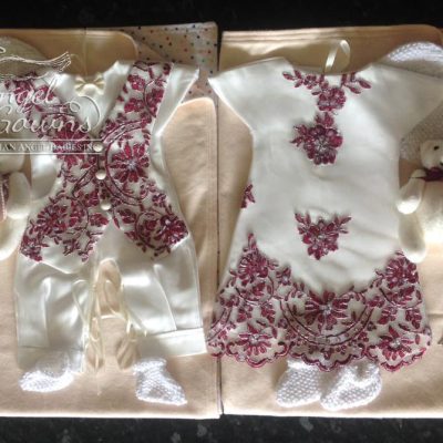 Two Angel Gowns packages with matching gowns, beanies, blankets, booties and keepsakes. One gown is a boy's romper with a vest in a lace design. The other gown is a girl's dress with the same lace used as embellishments.